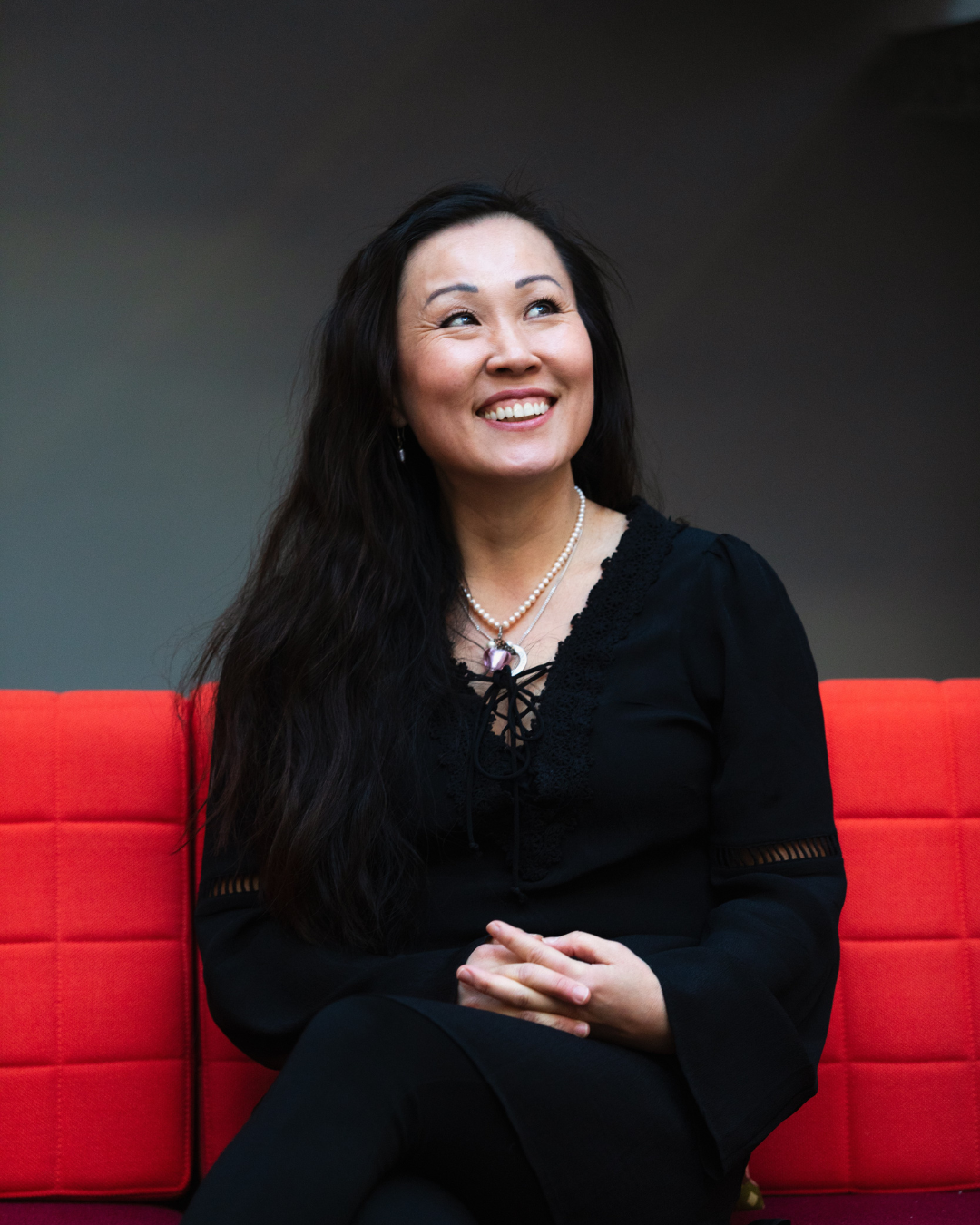 2 Photo: David Lagerlöf. Portrait of Jiang with hair down and black clothes. She's looking up, sitting in an orange sofa.